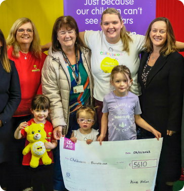 Group of adults and children smiling while holding a large cheque for €5610, awarded to ChildVision.