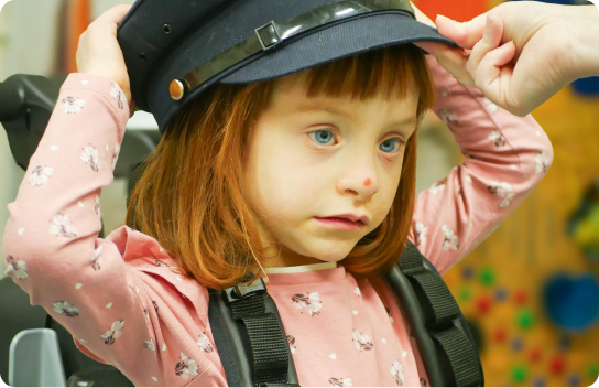Young girl wearing a pink shirt with white flowers wearing a black hat.