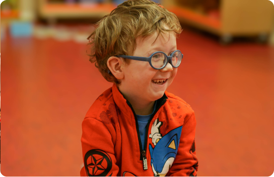 Young boy wearing a red sonic zip hoodie and blue round glasses smiling.